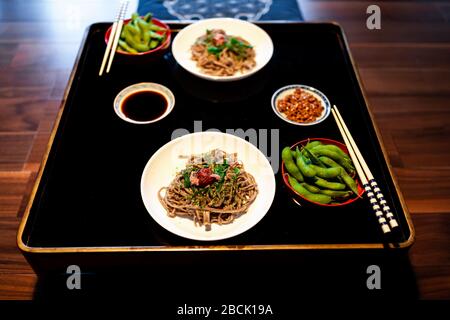 Blick auf traditionelles Japanisch im Ryokan Gäniseki mit Gemüsegericht aus gekochtem Edamame, Natto und Sojasoße auf Tellertasse mit Essstäbchen und Soba Stockfoto