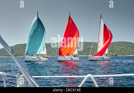 Segelboote nehmen bei Sonnenuntergang an einer Segelregatta Teil, sehen durch die Seile, Rennen von Segelbooten, Spiegelung der Segel auf dem Wasser, bunte Spinnaker, Insel Stockfoto