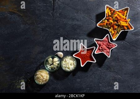 Getrocknete Pasta, Fleisch und Gemüse auf dunklem Schieferhintergrund mit Draufsicht und Kopierraum. Konzept Sternkomposition fusilli und bolognese Rezept. Stockfoto