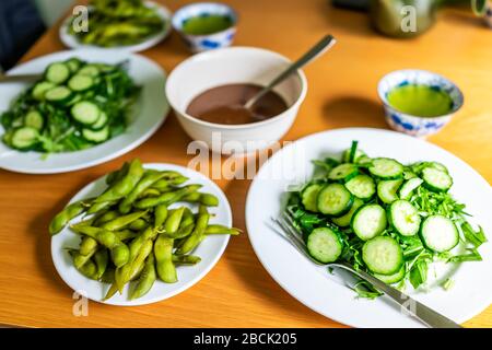 Holztisch und grünes Salatgericht mit japanischen Gurken und Mizuna-Grüns und gekochten Edamame Sojabohnen mit Tee zu Hause Mittag Abendessen Stockfoto