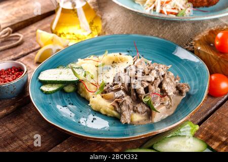 Fleischgulasch wird mit Kartoffelpüree und Gemüse auf einem Hintergrund aus Holztisch und Leinwandgewebe serviert Stockfoto