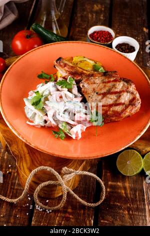 Schweinebraten, serviert mit Gemüse in Sauce auf dem Hintergrund eines Holztisches und Tischdecken Stockfoto
