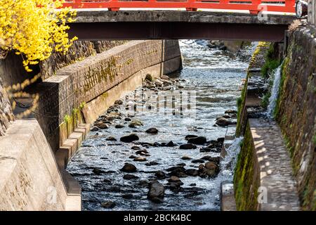 Kleine rote, bunte Brücke am Enako Fluss mit Felsen in Takayama, Präfektur Gifu in Japan mit Wasser im Frühling und gelbem Baum Stockfoto