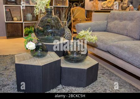 Das Innere des Hauses ist in Grau- und Brauntönen gehalten: Glasbecher mit getrockneten Blumen, Vase und Kerze auf einem Holztablett auf dem Kaffeetisch auf einem Sofa. M Stockfoto