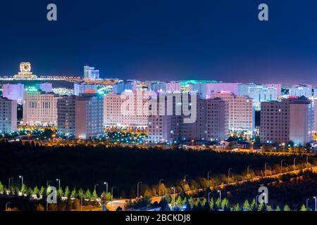 Aschgabat, Turkmenistan Skyline bei Nacht. Hochzeitspalast und Ashgabat Hotel sichtbar. Mehrere moderne weiße Marmorgebäude mit farbenfroher Beleuchtung. Stockfoto