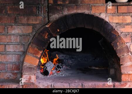 Feuer brennt im alten traditionellen Ziegelsteinofen zum Kochen. Kochen in einem Holzofen. Stockfoto