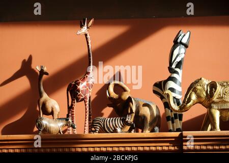 Geschnitzte afrikanische Tiere mit Seitenbeleuchtung, darunter Giraffen, Elefanten und Zebras. Stockfoto