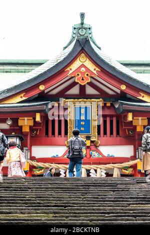 Tokio, Japan - 30. März 2019: Tor mit Menschen an der Eingangsfassade des Hie-Schrein-Tempels mit japanischem Architekturdach und Treppenstufen Stockfoto