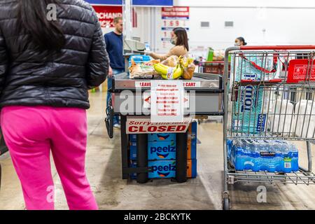 Sterling, USA - 1. April 2020: Personen im Costco Store bei der Kasse melden sich mit dem Einkaufswagen des Wassers, Papiertüchern, Lebensmitteln, Schild für wiederverwendbare Tütenverpackungen an Stockfoto