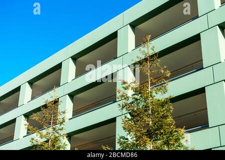 Parkhaus auf mehreren Ebenen, Fassade und Außenansicht. Grüne Vordergrundbäume. Blauer Himmel im Hintergrund. Stockfoto