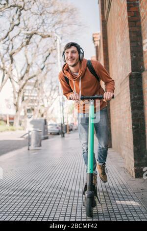 Porträt des jungen lateinmannes, der auf der Straße der Stadt einen Elektroscooter fährt. Modernes und ökologisches Transportkonzept. Stockfoto