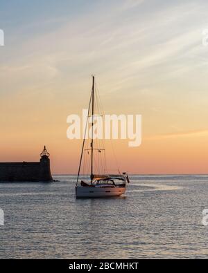 Segelyacht mit Segeln hinunter in den Hafen von Collioure am Mittelmeer Küste von Südfrankreich bei Sonnenuntergang Stockfoto