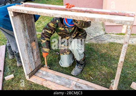 Menschen, die in der Ukraine an einem Gemüsewintergarten für einen erhöhten Bettenkälterahmen arbeiten, dacha mit einem Hammer für die Haltemaschine Stockfoto