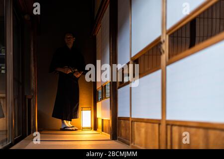 Japanisches Ryokan traditionelles Haus mit Mann in Kimono yukata mit Tabi geta Schuhen, die von Shoji Schiebetüren und Tatami-Mattenboden stehen Stockfoto