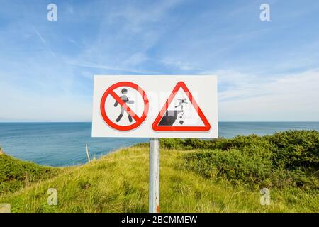 Ein Schild, das die Besucher warnt, vorsichtig zu gehen und zerfallende Felsen auf der Klippe am Kampfplatz des zweiten Weltkriegs von Pointe du hoc in der Normandie, Frankreich, zu vermeiden Stockfoto