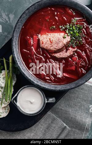 Ukrainische und russische traditionelle Rote Bete Suppe - Borscht in Schüssel mit Rippenauge Fleisch, Roggenbrot, Scheiben Speck und saure Sahne auf Holzgrund Stockfoto