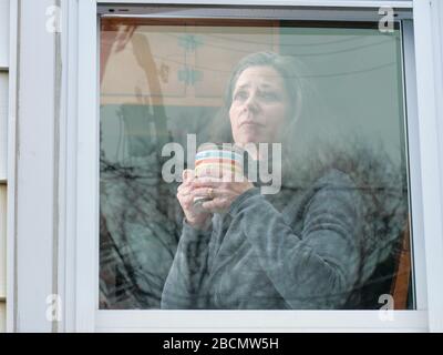 Oak Park, Illinois, USA. April 2020. Eine Frau schaut ihr Küchenfenster während der COVID-19-Unterschlupf-in-Place-Bestellung aus. Zu Hause festsitzen kann Gefühle der Isolation und Einsamkeit hervorrufen. Stockfoto