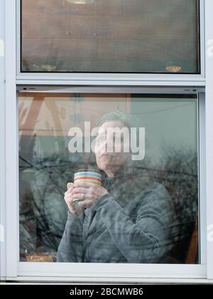 Oak Park, Illinois, USA. April 2020. Eine Frau schaut ihr Küchenfenster während der COVID-19-Unterschlupf-in-Place-Bestellung aus. Stockfoto