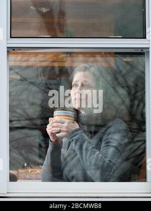 Oak Park, Illinois, USA. April 2020. Eine Frau schaut ihr Küchenfenster während der COVID-19-Unterschlupf-in-Place-Bestellung aus. Stockfoto