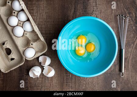 Drei gesprungene Eier in blauer Mischschale, Eierschalen, ganze Eier in Kartonkarton, Metall-Schneebesen, Holztisch Stockfoto