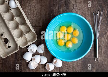 Acht gesprungene Eier in blauer Mischschale, Eierschalen, ganze Eier in Kartonkarton, Metall-Schneebesen, Holztisch Stockfoto