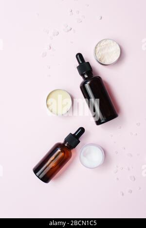 Glasflaschen mit feuchtigkeitsspendenden Serum, Sahne- und Balzgläschen auf pinkfarbenem Pastellhintergrund. Hausgemachte Hautpflege. Copyspace, Vorlage. Stockfoto