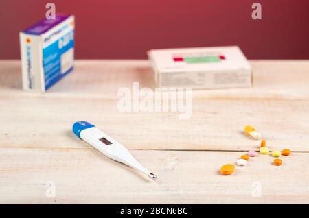 Heimtherapie. Digitalthermometer, mehrere Pillen Boxen und verschiedene bunte Pillen im Vordergrund Stockfoto