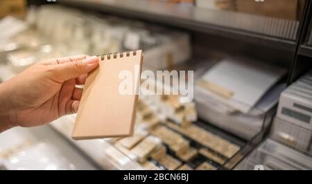 Leeres braunes Papierblatt mit Notizbuchpapier ohne Zeile zum Schreiben von Textnotizen. Die Hand eines Weibchens hielt ein Buch mit leerem Papier auf einem braunen Korkbezug Stockfoto