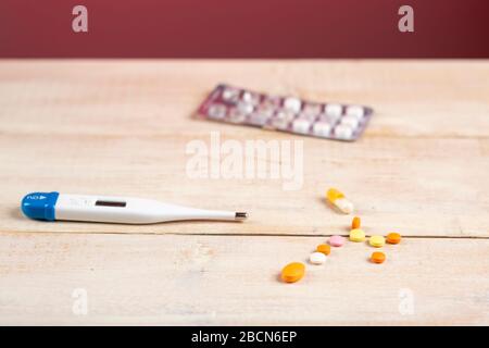 Heimtherapie. Digitalthermometer, gelbe und orange Pillen und gebrauchte Blister mit runden weißen Pillen Stockfoto