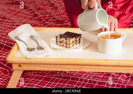 Tasse Kaffee mit Milch und Schokoladenkuchen. Süßes köstliches Frühstück auf einem Tisch mit Betttablett Stockfoto