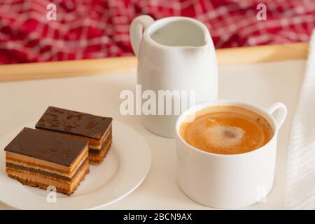 Tasse Kaffee mit Milch und Schokoladenkuchen. Süßes köstliches Frühstück auf einem Tisch mit Betttablett Stockfoto