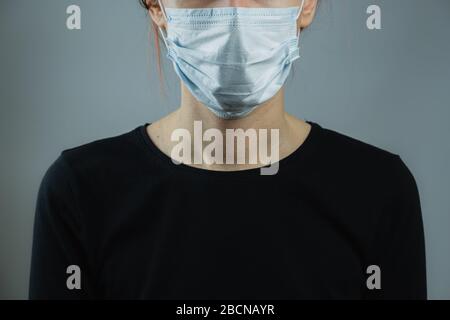 Weibliche Person in einer chirurgischen Maske, minimalistisches und generisches Bild. Personenschutz bedeutet vor Viren oder Keimen, vor schwachem Hintergrund Stockfoto
