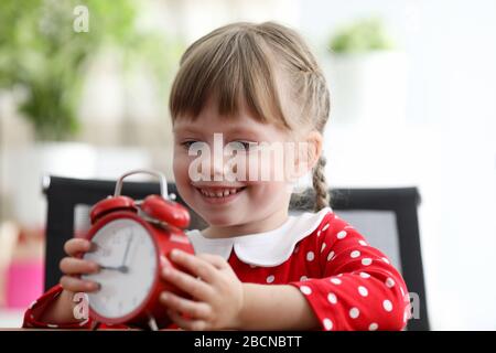 Tochter sitzt am Tisch und hält einen Wecker Stockfoto