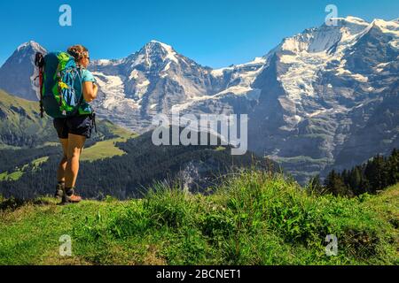 Fröhlicher sportlicher, aktiver Frauenhiker mit farbenfrohem Rucksack und Bergausrüstung, der die Aussicht in atemberaubenden Bergen, Murren, Berner Oberland, SW genießt Stockfoto