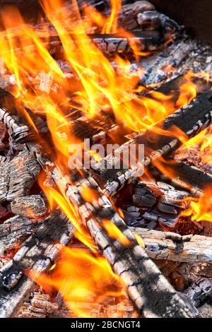 Holzfeuer Hintergrund. Schwarzes verbranntes Holz mit orangefarbenen Flammen und Glut im Nahaufnahme. Vertikales Bild. Stockfoto