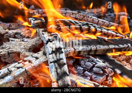 Holzfeuer Hintergrund. Schwarzes verbranntes Holz mit orangefarbenen Flammen und Glut im Nahaufnahme. Stockfoto