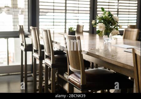 Leere Holzstühle mit Lederpolsterung sind um die Tische im Restaurant herum aufgestellt. Cafe geschlossen während covid-2019 Quarantäne. Stockfoto