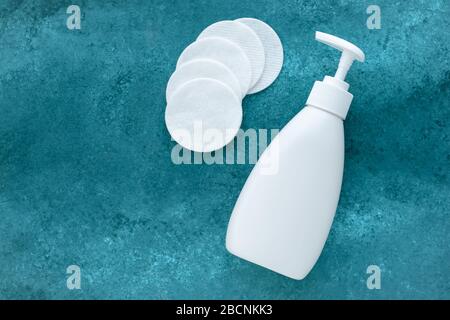 Gesichtstonika in weißer Spenderflasche und viele Baumwollscheiben auf Aqua-Hintergrund. Kunststoffflasche mit Flüssigkeit. Text, Kopierbereich. Makeup Remover, Produkt o. Stockfoto
