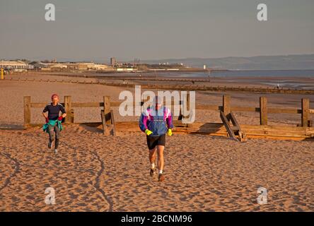 Portobello, Edinburgh, Schottland, Großbritannien. 5.. April 2020. Sonnenaufgang am Portobello Beach, dargestellt von Mann und Frau beim Laufen, mit verschiedenen Leuten, die schwimmen, spazieren gehen und in Kontemplation am Sandstrand sitzen. Stockfoto