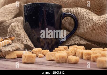 Dunkelblauer Teebecher aus Keramik, Plätzchenstöcke mit Schokolade und weißer Vereisung sowie braune Rohrzuckerstücke auf Holzhintergrund. Nahaufnahme Stockfoto