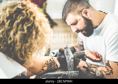 Der junge Tattoo-Künstler, der in seinem kreativen Atelier arbeitet - Tattoist bei der Arbeit - zeitgenössische Hauttrends - konzentriert sich auf seinen Kopf Stockfoto