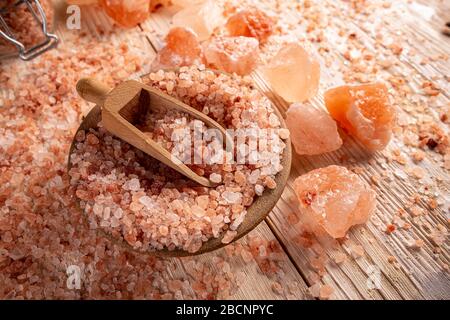 Große Kristalle aus rosafarbenem Himalayasalz in Holzschale mit Schaufel auf Holzbrett Stockfoto