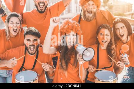 Orangefarbene Sportfans schreien, während sie ihre Mannschaft aus dem Stadion unterstützen - Fußballfans, die Spaß an der Competion Event haben - Meister und Sieger Stockfoto