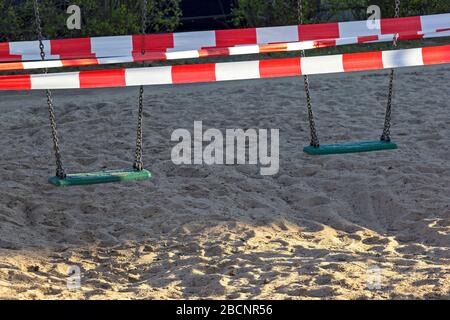 Blick auf einen geschlossenen Spielplatz. Die Schaukel wird mit einem Absperrband verschlossen. Im Zuge der Koronakrise gibt es zahlreiche Kontaktbarrieren und Kinder Stockfoto