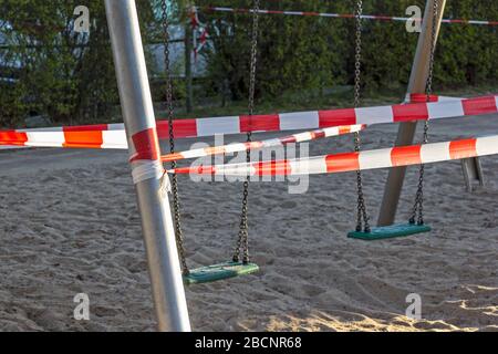 Blick auf einen geschlossenen Spielplatz. Die Schaukel wird mit einem Absperrband verschlossen. Im Zuge der Koronakrise gibt es zahlreiche Kontaktbarrieren und Kinder Stockfoto