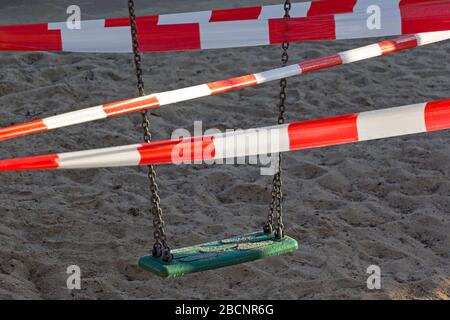 Blick auf einen geschlossenen Spielplatz. Die Schaukel wird mit einem Absperrband verschlossen. Im Zuge der Koronakrise gibt es zahlreiche Kontaktbarrieren und Kinder Stockfoto