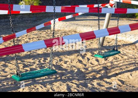 Blick auf einen geschlossenen Spielplatz. Die Schaukel wird mit einem Absperrband verschlossen. Im Zuge der Koronakrise gibt es zahlreiche Kontaktbarrieren und Kinder Stockfoto