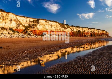 Sonnenuntergang am Strand von Hunstanton im Norden von Norfolk im Osten von Anglia, der die farbenfrohe Felswand und den Leuchtturm in den Ebbe-Pools beleuchtet Stockfoto