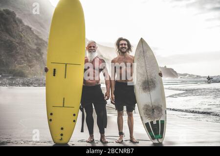 Mehrgenerationige Freunde, die am tropischen Strand surfen - Familienmitglieder haben Spaß am Extremsport - fröhliches älteres und gesundes Lifestyle-Konzept Stockfoto