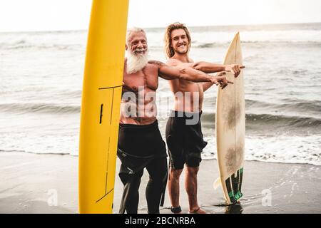 Mehrgenerationige Freunde, die am tropischen Strand surfen - Familienmitglieder haben Spaß am Extremsport - fröhliches älteres und gesundes Lifestyle-Konzept Stockfoto